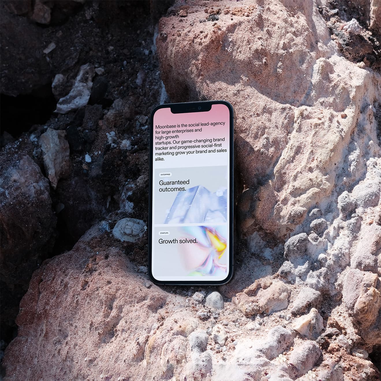 Moonbase's mobile website displayed on a phone resting against pale textured rocks.